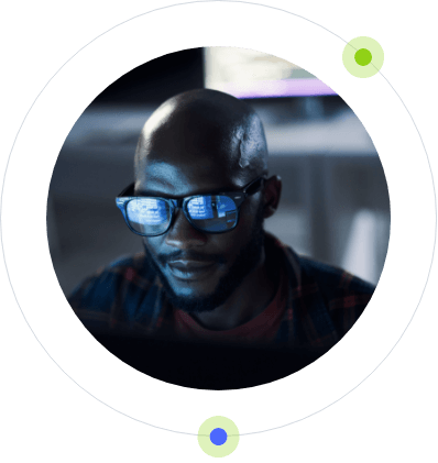A focused bald man wearing glasses, with the reflection of a computer screen visible on the lenses, framed within a circle augmented by green dots within the Post-RiskIQ SOC.