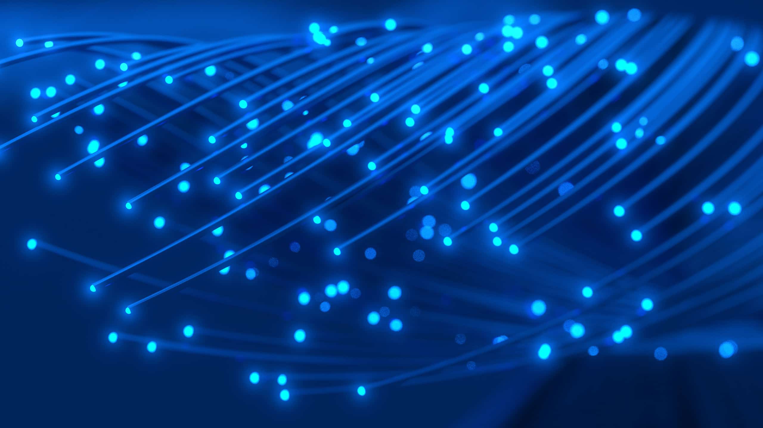 Glowing blue optical fibers spread out against a dark blue background, with light points scattered across the fibers, illustrating technology and data transmission.