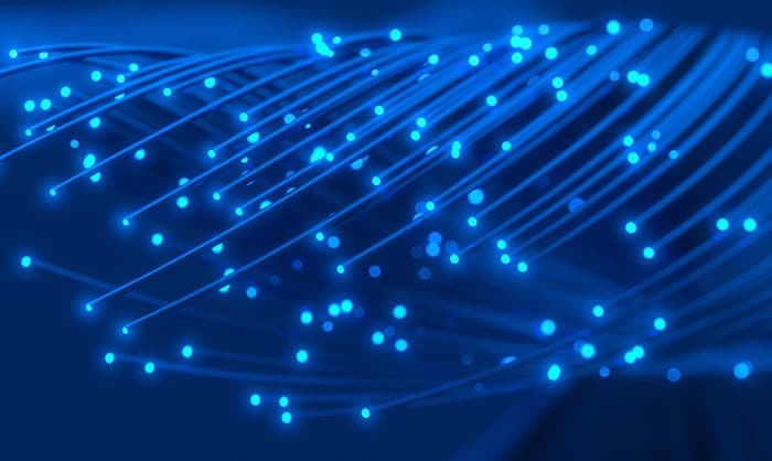 A close-up image of optical fibers illuminated with blue light, showcasing multiple glowing points along the cables against a dark blue background.