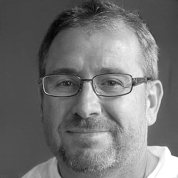 Black and white portrait of a smiling middle-aged man with glasses, short hair, and a beard. he is wearing a light-colored shirt and looking directly at the camera.