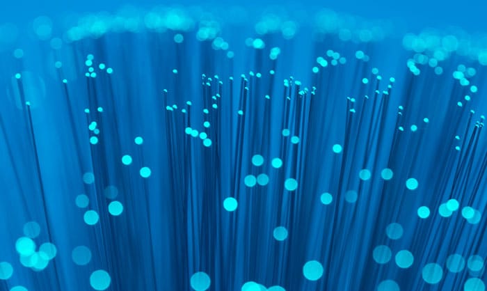 A close-up image of numerous glowing fiber optic cables in shades of blue, illustrating data transmission and modern technology.