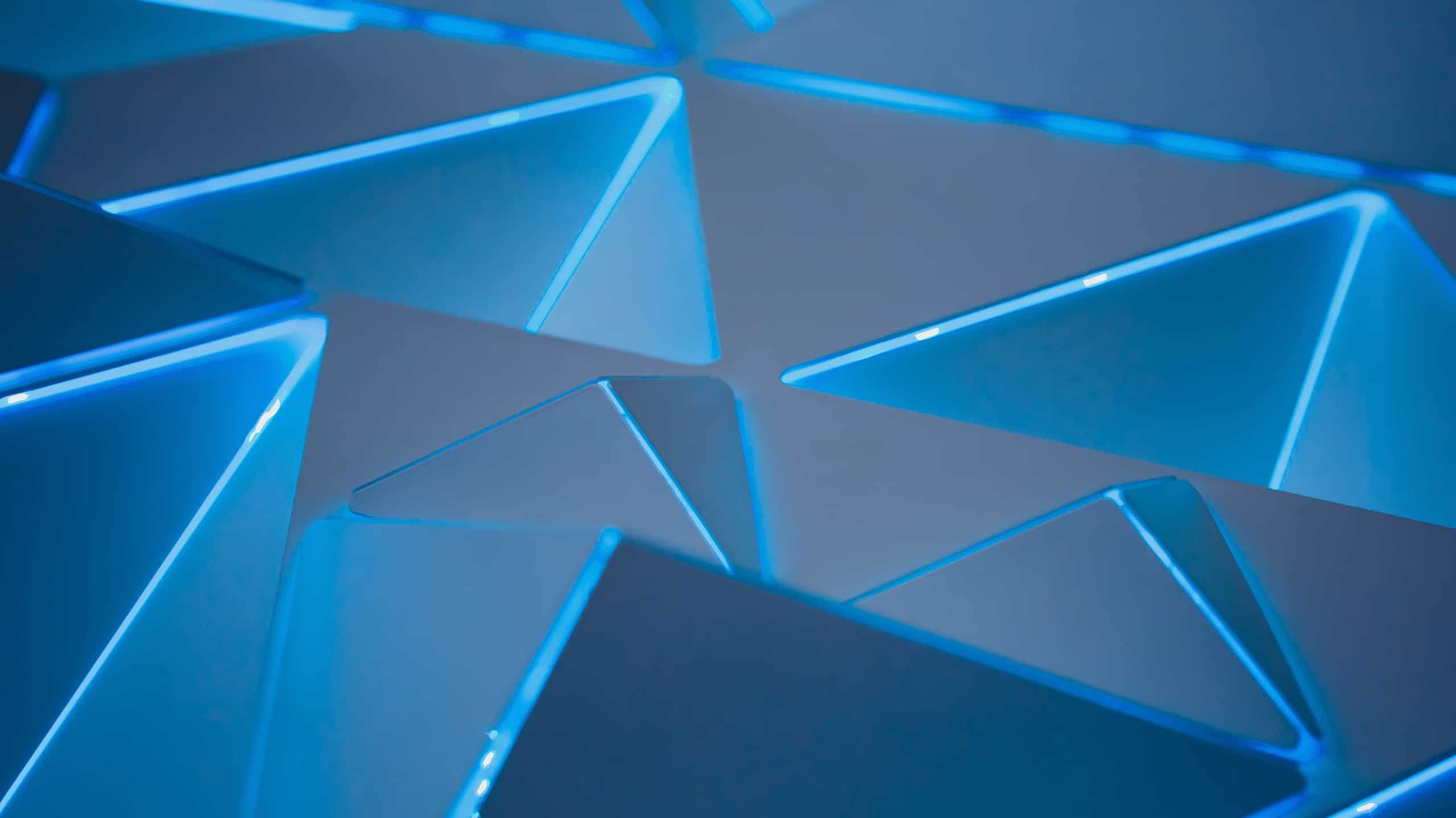 Abstract image featuring a pattern of overlapping blue triangles with soft lighting, creating a futuristic and geometric aesthetic.