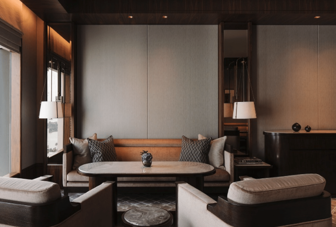 A luxurious living room with elegant decor, featuring a large sofa with decorative pillows, two armchairs, a sleek coffee table, and pendant lights. The room has a warm, neutral color scheme and large windows that let in natural light.