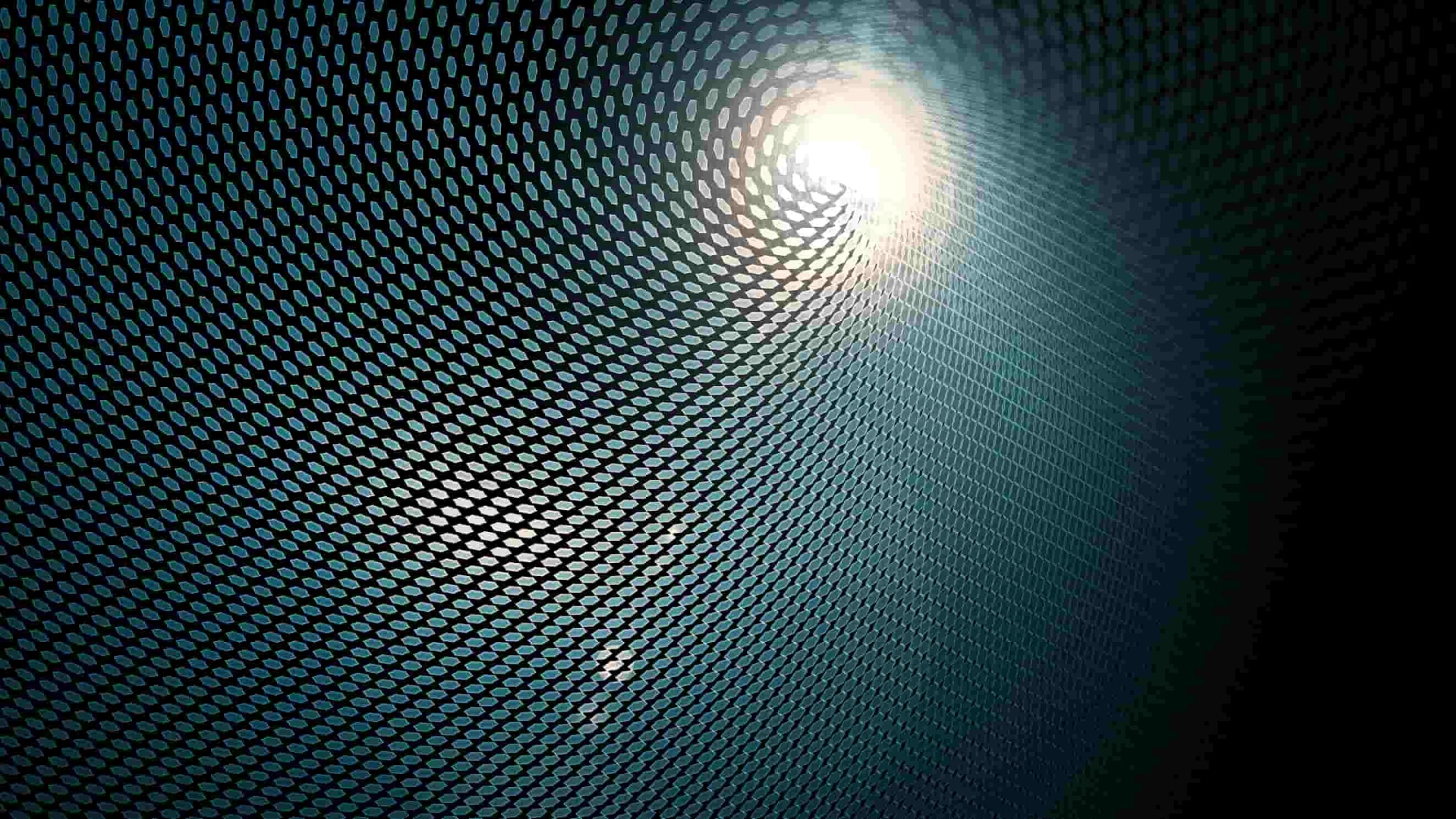 Sunlight shining through a perforated metal surface, creating a pattern of circular light spots on a dark background.